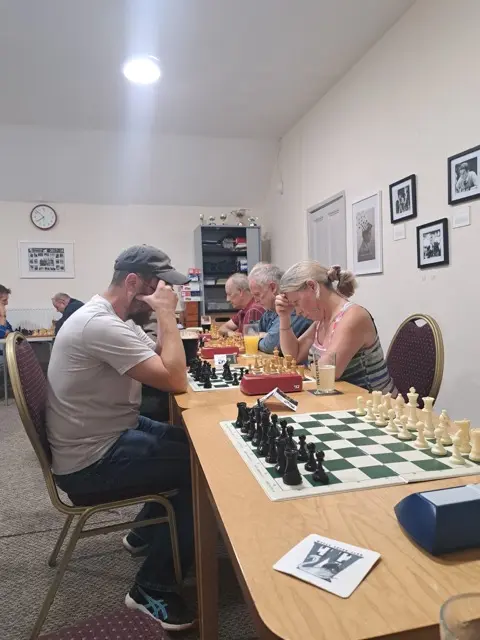 Players concentrating over their boards along a row of tables
