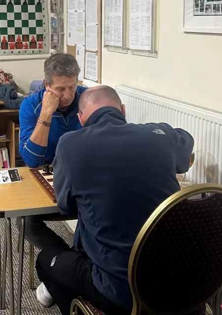 A player resting his head on his hand at board 1 while his opponent studies the position